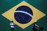 A man checks his mobile phone as a woman riding a bike passes next to a big Brazilian flag in Sao Paulo, Brazil June 28, 2018